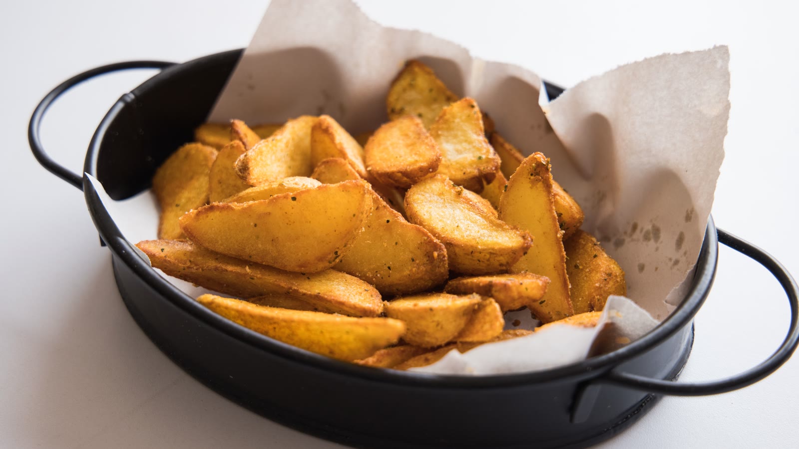 Sprøde kartoffelbåde i et sort fad med bagepapir