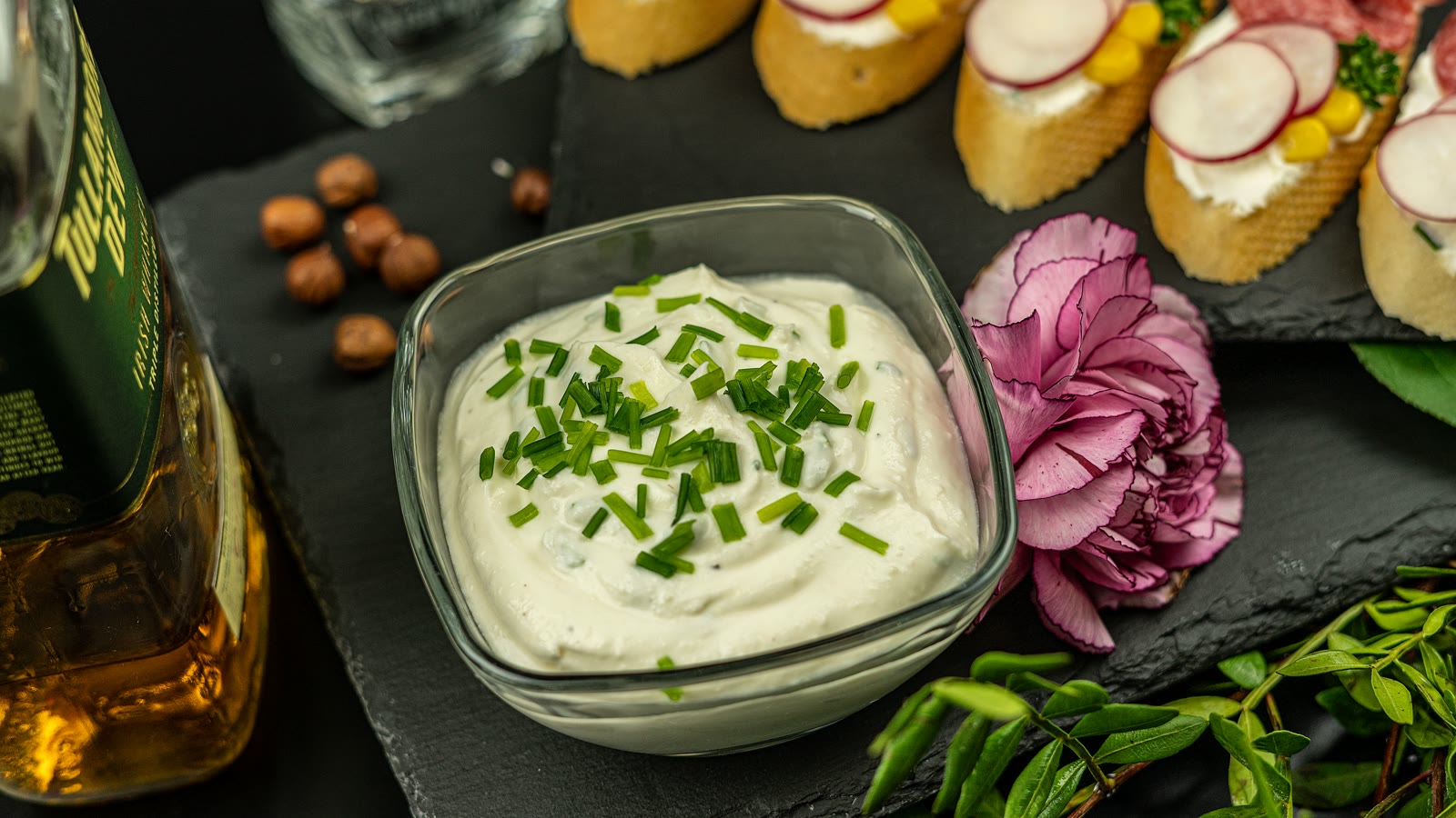 Kold creme med hakkede purløg i en glasskål ved siden af små snitter